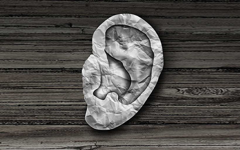 A crumpled piece of white paper cut into the shape of an ear rests on a dark wooden surface with visible grain patterns.