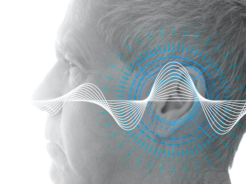 A side profile of an older man’s face with digital blue and white waveforms and circular graphics superimposed over his ear, symbolizing hearing, sound waves, or auditory technology.